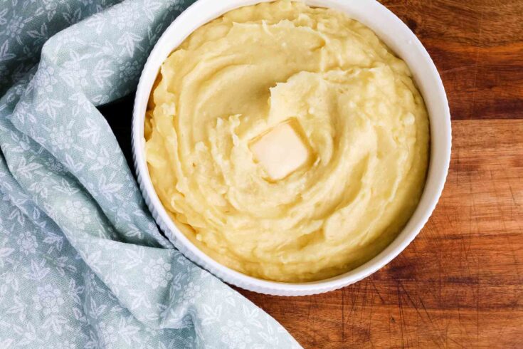 white bowl of mashed potatoes on wood cutting board with pad of butter on top