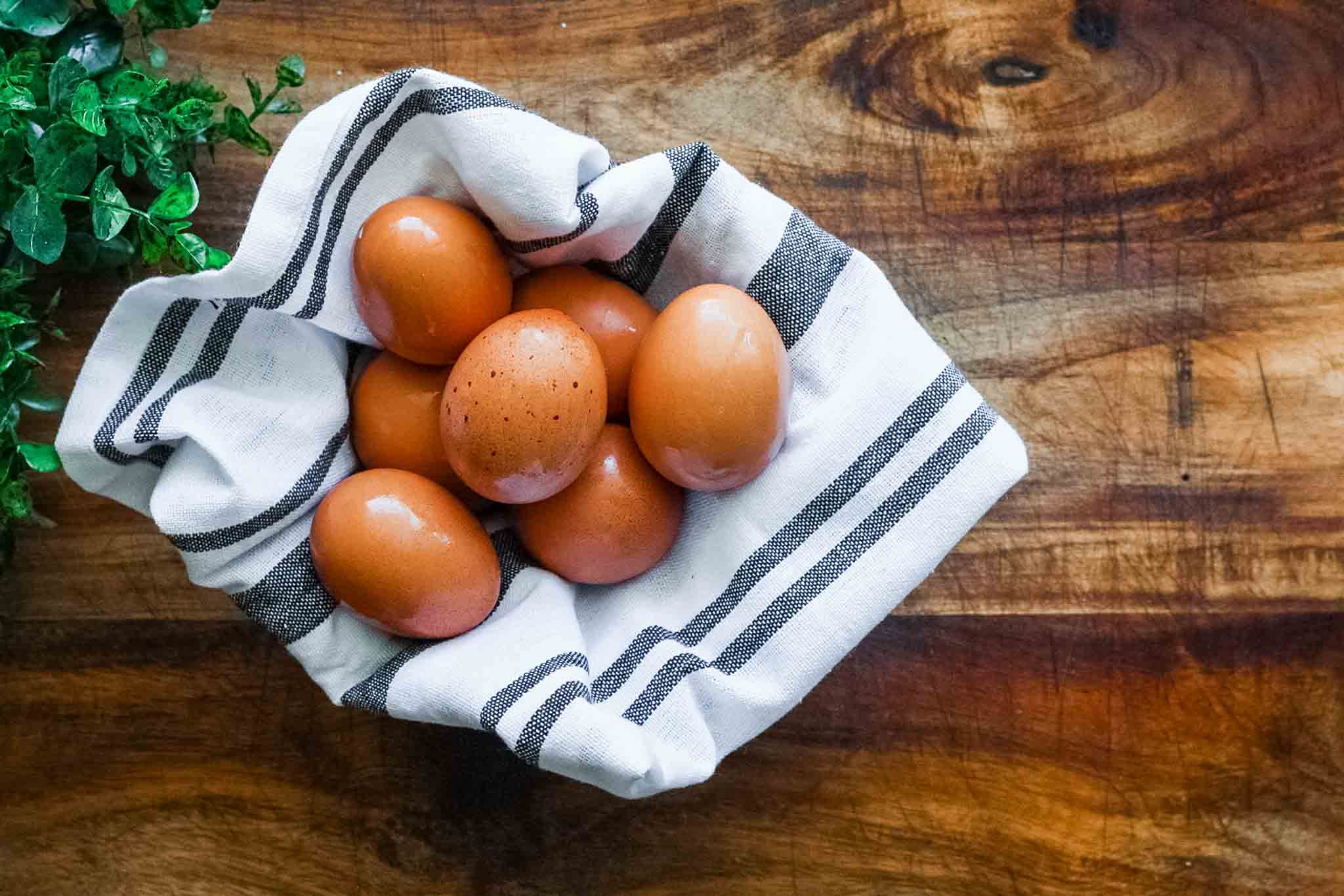 hard boiled eggs in a glass bowl with black and white striped dish towel on a wood cutting board