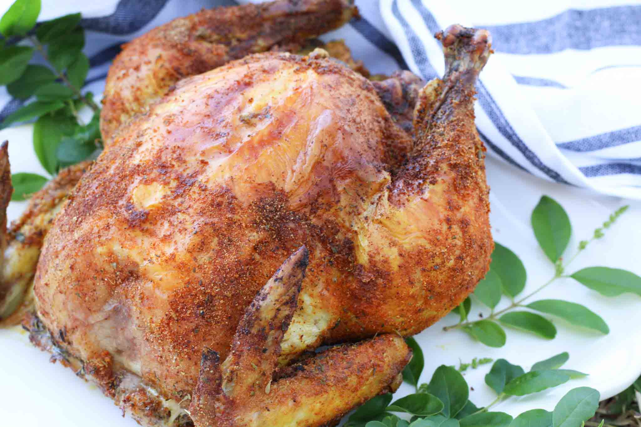 crispy whole chicken next to greenery and blue and white dish towel
