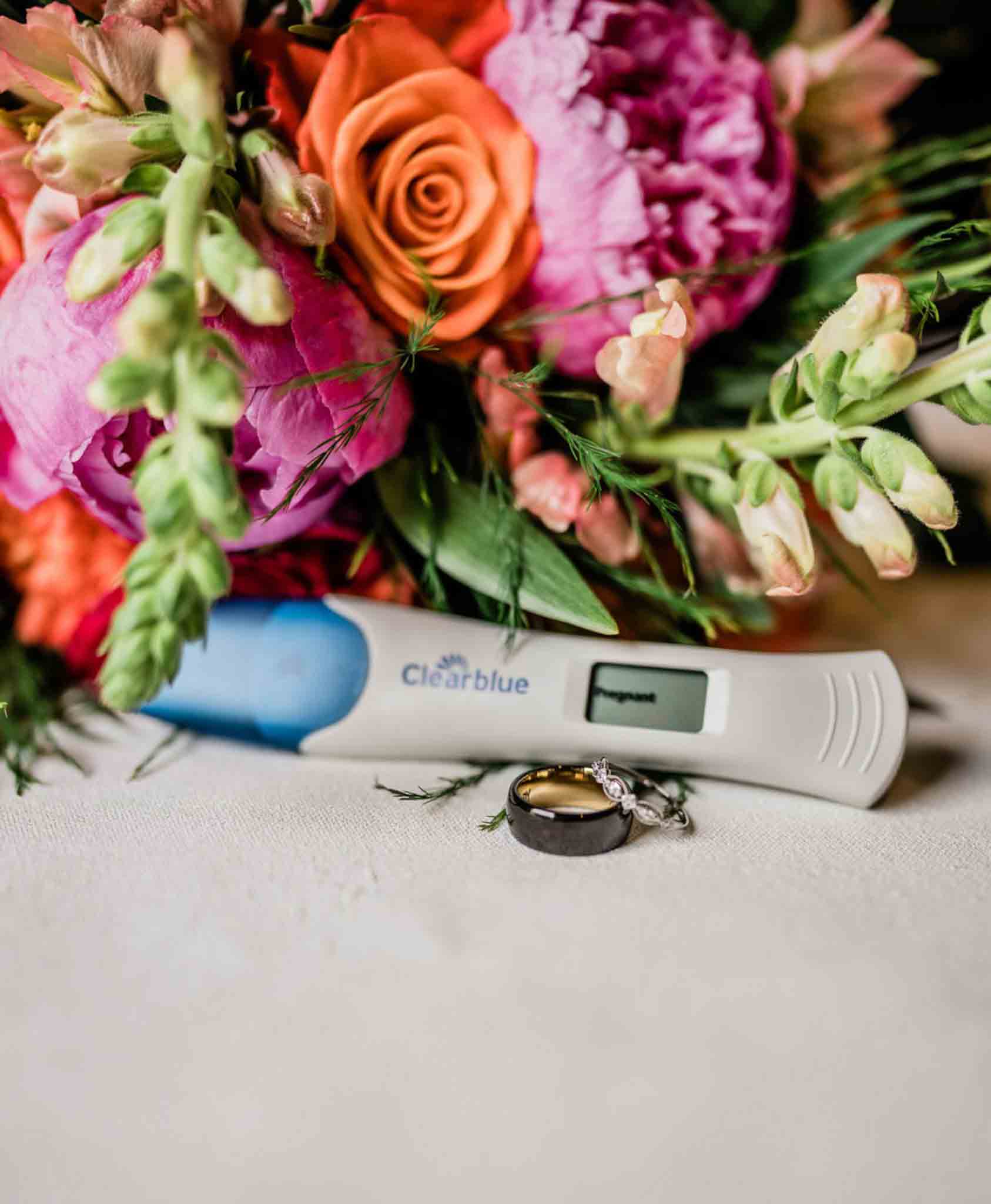 digital pregnancy test on table with wedding bands and pink flowers