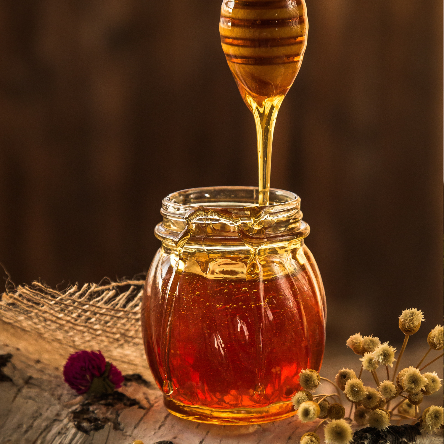 glass jar of honey next to flowers